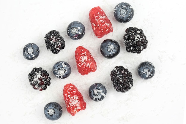 Blueberries, blackberries, gooseberries and raspberries sprinkled with coconut on white background. healthy fresh vegetables and food