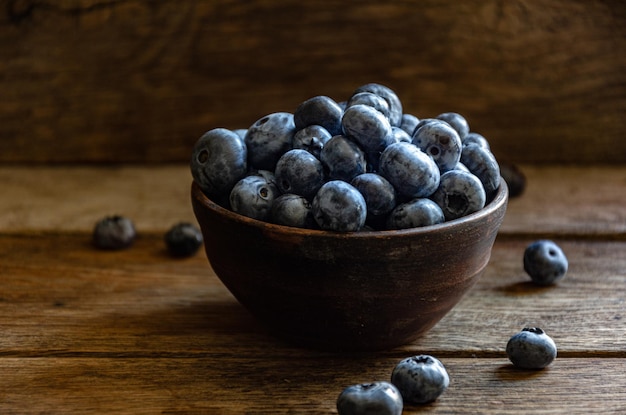 木製のテーブルの上に、粘土のカップに入ったブルーベリー。キッチンで熟した果実を収穫します。