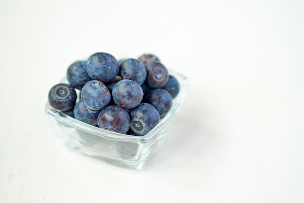 Blueberries in a glass cup on a white wooden background.