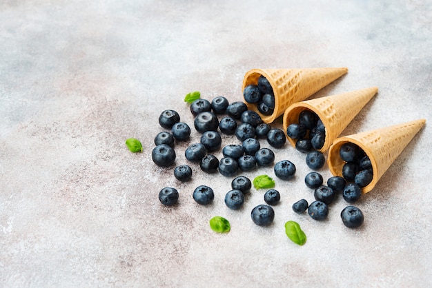 Blueberries lie in a waffle cone and scattered on a concrete table. Summer seasonal product. Healthy vegetarian dessert.