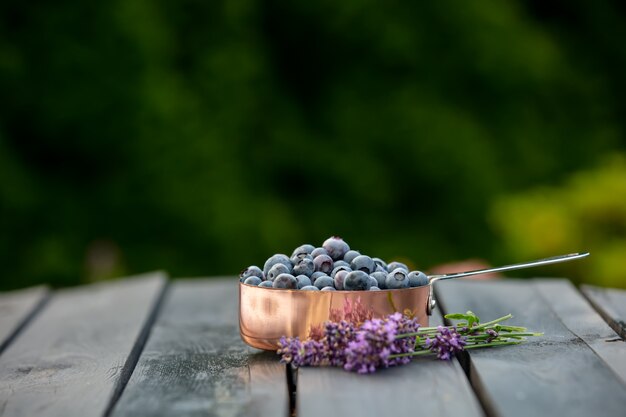 庭の木製のテーブルの周りの金属鍋とラベンダーの花のブルーベリー