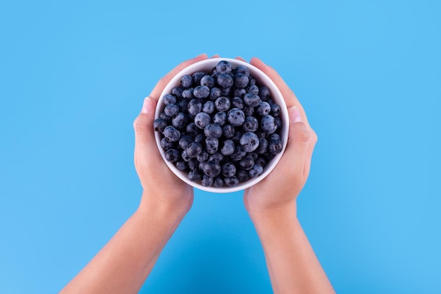 Blueberries in a white bowl in the hands of an unrecognizable woman