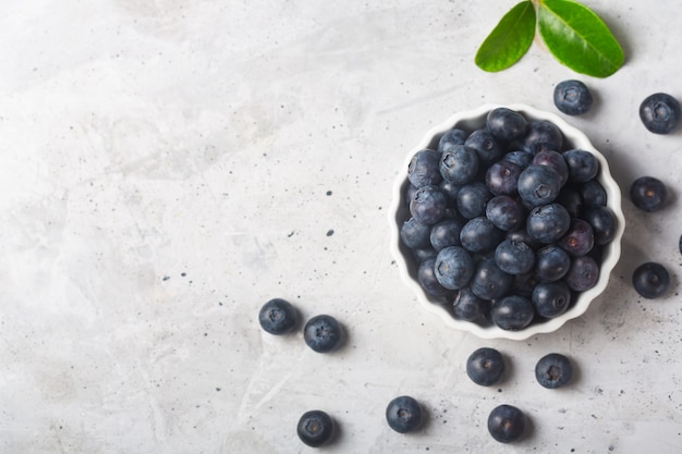 Blueberries in a white bowl with a leaf on a concrete background