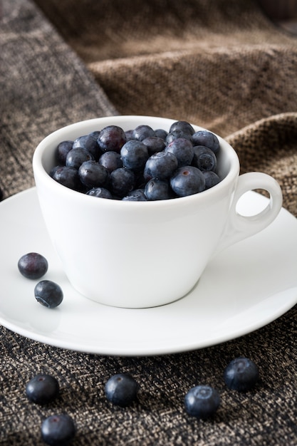 blueberries in a white cup on a brown cloth