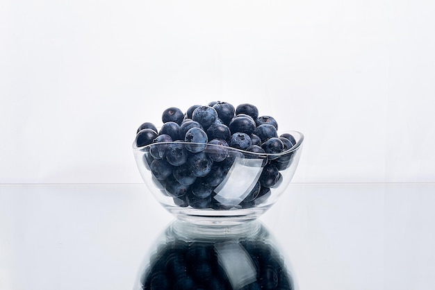 Blueberries on a white mirror background in a glass bowl