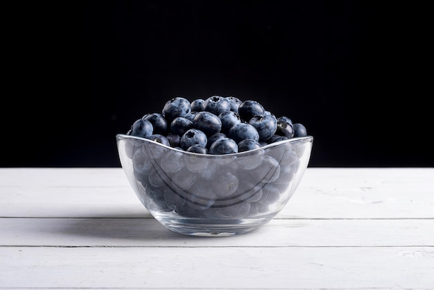 Blueberries on a white table with a black background in a bowl on a wooden table