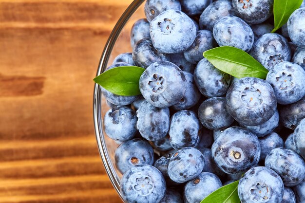 Blueberries with green leaves in a glass plate and water drops on a wooden background