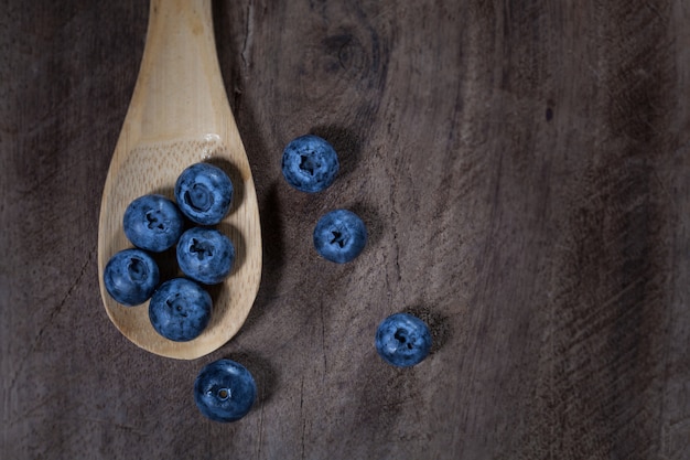 Photo blueberries in a wooden spoon placed on a wooden table, taken from above.