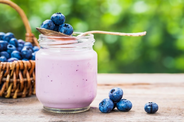 Blueberries yogurt in jar basket of berries and saucer with bilberries on table outdoors