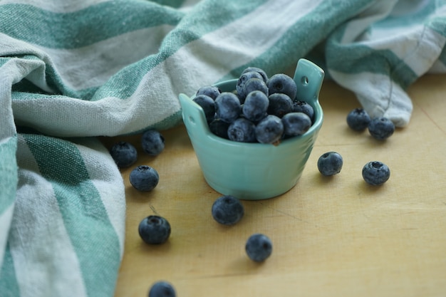 Blueberry berries in a clay white small bowl on a light wooden Board with a light green striped cloth kitchen napkin