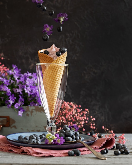 ягоды черники в вафельном стаканчике в окружении фиолетовых цветов и ягод. Летняя тема. левитация