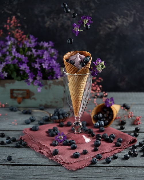 Blueberry berries in a waffle cup surrounded by purple flowers\
and berries. summer theme. levitation