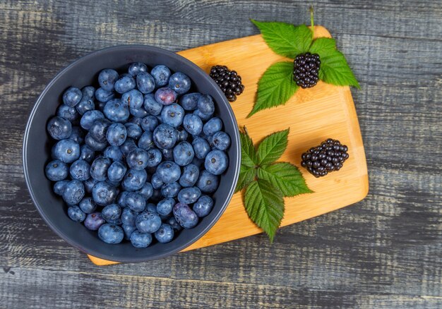 Blueberry berry in donkergrijze keramische kom op houten snijplank op donkerblauwe houten achtergrond