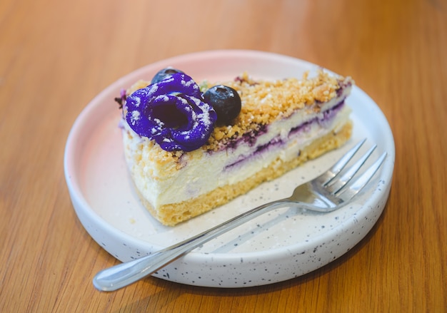 Blueberry cheesecake piece in the white dish on wooden table.