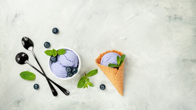 Blueberry ice cream cone with mint leaves on gray surface. Top view, copy space