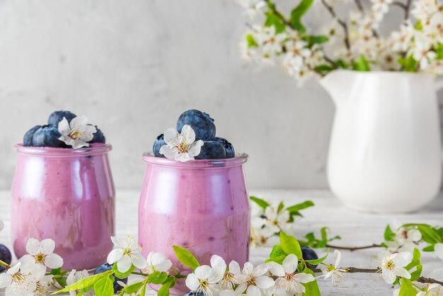 Черничный йогурт в бокалах подается со свежей черникой и весенними цветами вишни в вазе