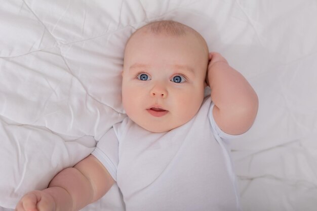 Blueeyed baby in a white bodysuit lies in a crib and looks at the camera