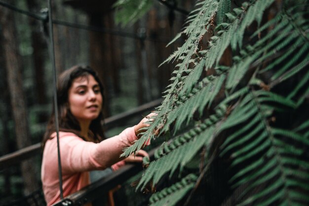 Photo blueeyed caucasian girl in pink shirt on platform touching exotic leaf of green plant in lush forest