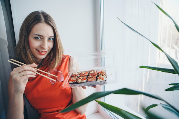 Foto ragazza caucasica blueeyed in vestito dal cinese tradizionale che mangia i bastoni dei sushi.