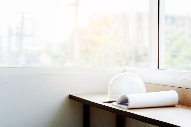 Photo blueprints with hardhat on wooden table by window