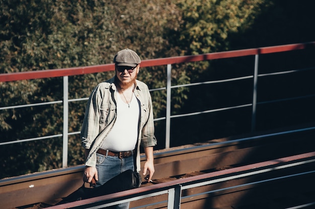 Bluesman met gitaarkoker rookt sigaretten op spoorweg. Bluesmuzikant met sigaret op spoorweg. Coole kerel met gitaar. Bebaarde man reist licht. Wandelende hippie levensstijl. Excentrieke roker.