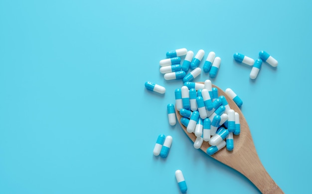 Bluewhite capsule pills on wooden spoon Capsule pills on blue background Health topics Drug