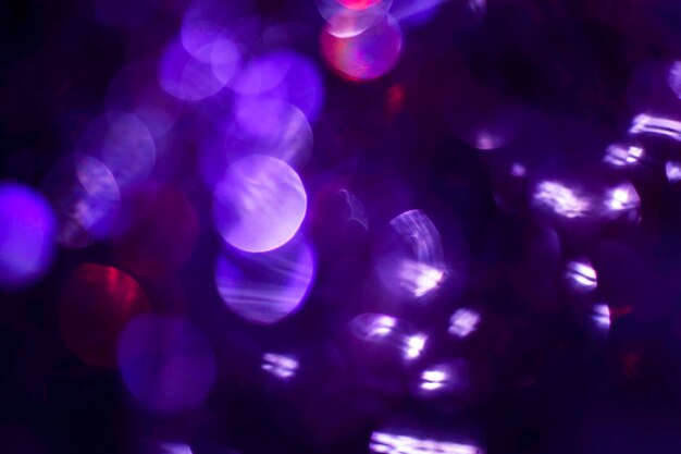 ぼやけた抽象的な紫のキラキラテクスチャ、黒の背景に焦点がぼけたクリスマスライト。休日のクリスマスのコンセプト。