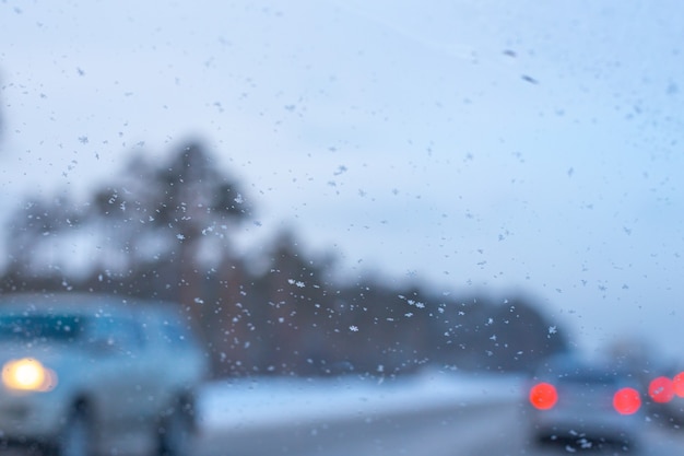 Blurred background of a car windshield with snowflakes and cars in the background