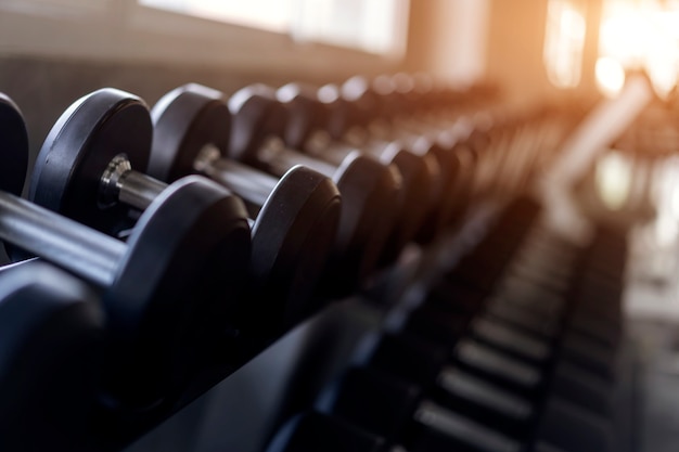 Blurred background of Rows of black dumbbells on rack in the gym