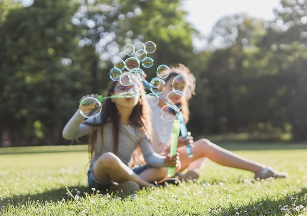 Blurred background two caucasian girlssisters blowing soap bubbles in the park