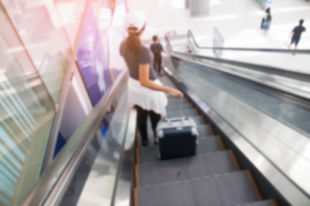 Blurred background of woman standing on escalator with luggage suitcase