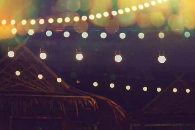 Blurred bokeh light with yellow string lights decor in beach restaurant at dusk of summer background