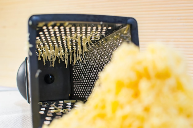 Blurred bunch of grated cheese on the background of a metal grater kitchen