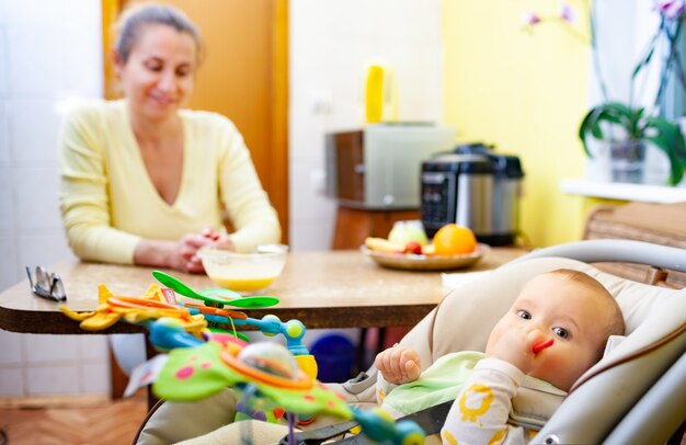 Blurred charming smiling mom sits at the table and rejoices at her little cheerful newborn baby girl