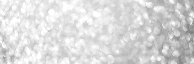 Blurred defocused bokeh banner with Christmas lights and silver glitter sparkles. Silver abstract background