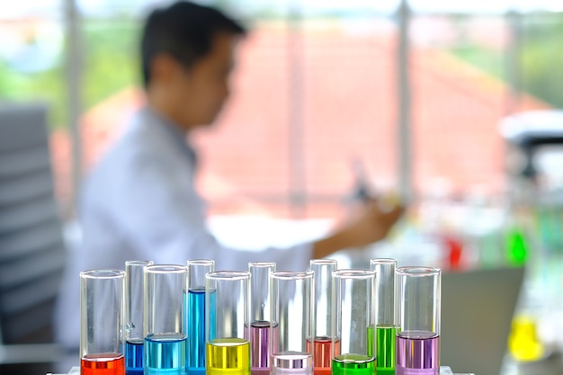 Blurred doctor sit analyzing in laboratory room have color testing glass straw foreground.