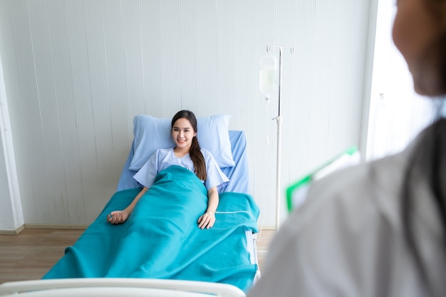 Foto sfocato di consulenza terapeutica di una dottoressa con emozioni positive per una giovane paziente asiatica con un sorriso sul letto in background dell'ospedale