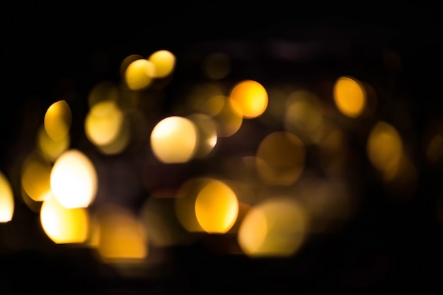 Blurred gold bokeh on black background. Glowing yellow lights bokeh in the dark, reflections