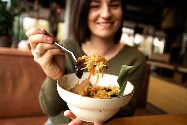 彼女のおいしい食事を見せて、笑顔でぼやけた幸せな女性。アジア料理のコンセプト。