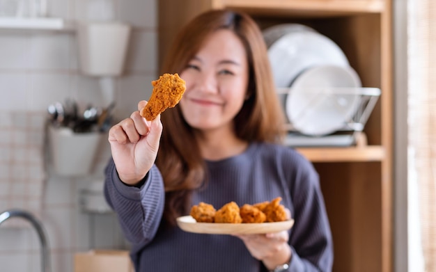 Immagine sfocata di una bella giovane donna asiatica che tiene e mostra un piatto di pollo fritto in cucina a casa