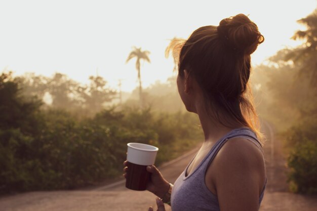 Blurred image of a woman holding a cup of coffee in the middle of nature.