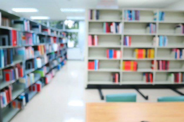 Blurred of the interior of the public library with wooden tables, chairs and books in bookshelves.