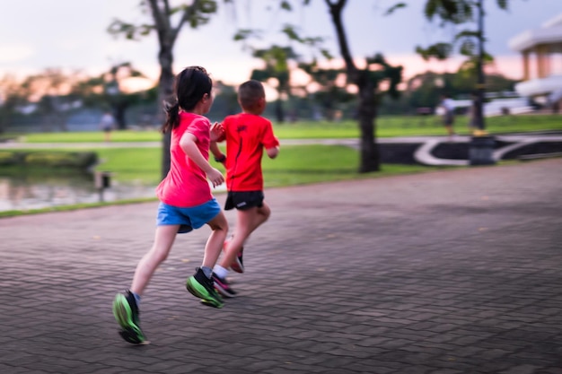 Blurred motion concept brother and sister running in the summer park on sunset.