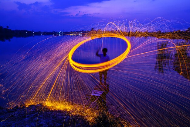 Blurred motion of person standing by illuminated light against sky at night