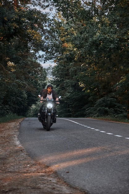 Movimento sfocato un giovane motociclista in un casco cavalca rapidamente ad alta velocità su una strada forestale in movimento