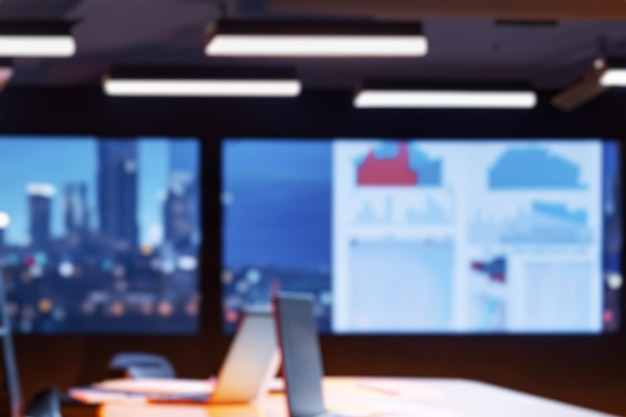 blurred office background modern empty meeting room with big conference table with various documents and laptop on it wall tv showing company statistics graphs late evening or night city outside