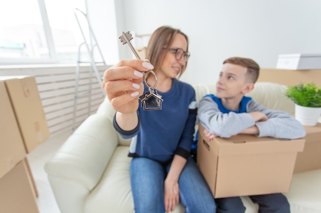 Blurred positive mom and son are sitting on the couch and showing the keys to the new apartment