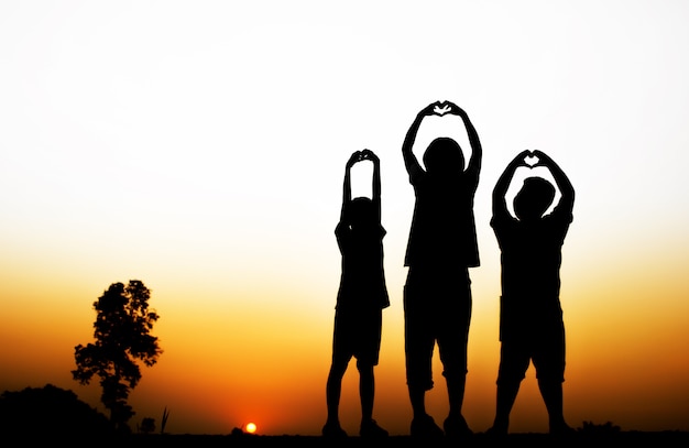 Photo blurred silhouette of children make heart with beautiful sunset background.