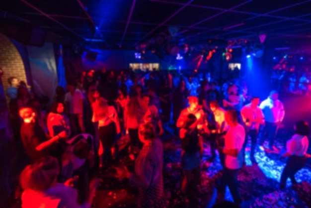 Фото Размытые силуэты группы людей, танцующих в ночном клубе на танцполе под яркими прожекторами