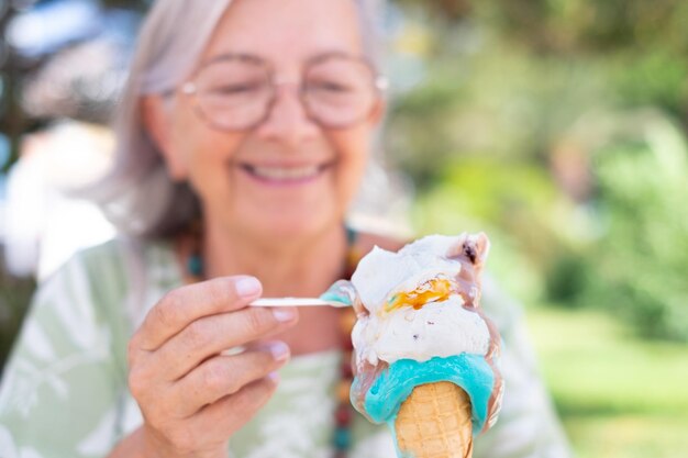 Blurred smiling senior woman eating a melting ice cream cone enjoying sweet food and summer time